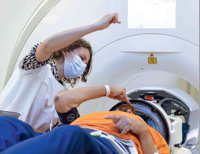 Le patient est dans un scanner IRM. Une soignante est à côté de lui.