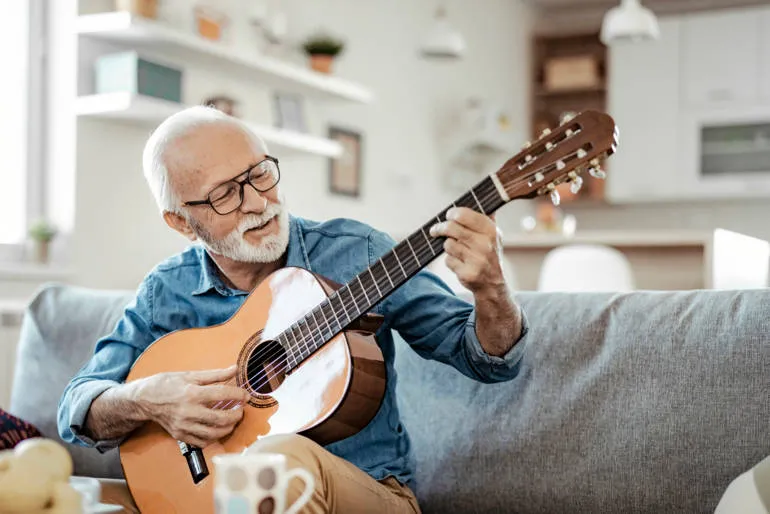 Personne senior avec barbe et lunettes qui joue de la guitare