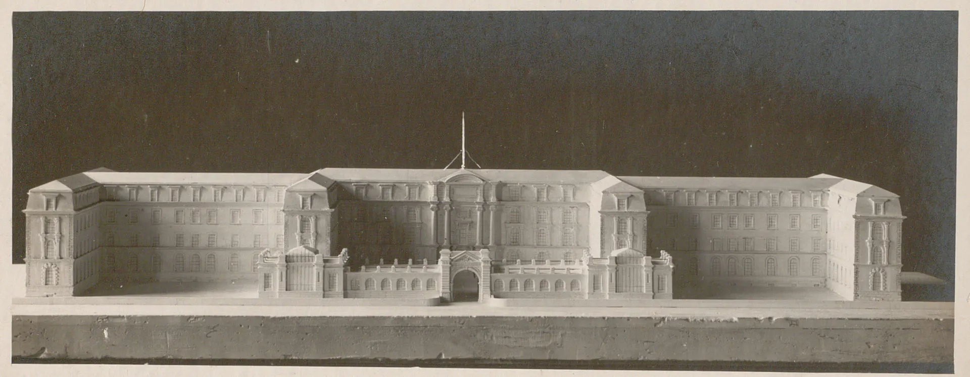 Maquette blanche d'un immeuble à plusieurs ailes avec un mât sur le toit.