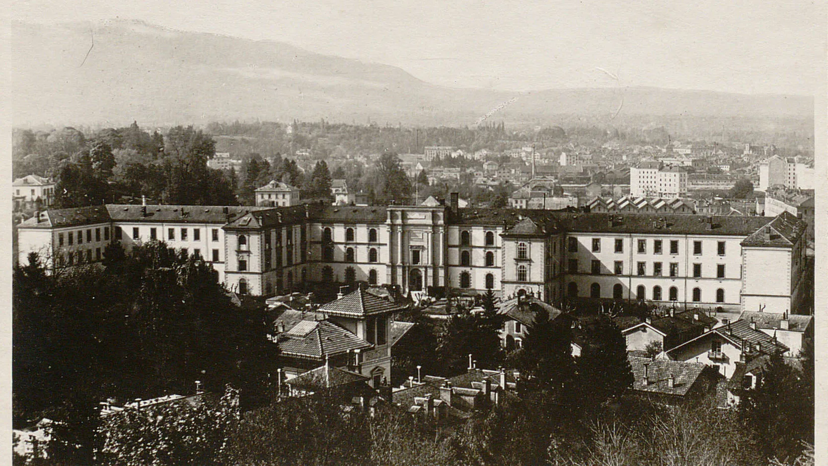 Un grand bâtiment à plusieurs ailes avec une entrée monumentale, des plus petites maisons autour.