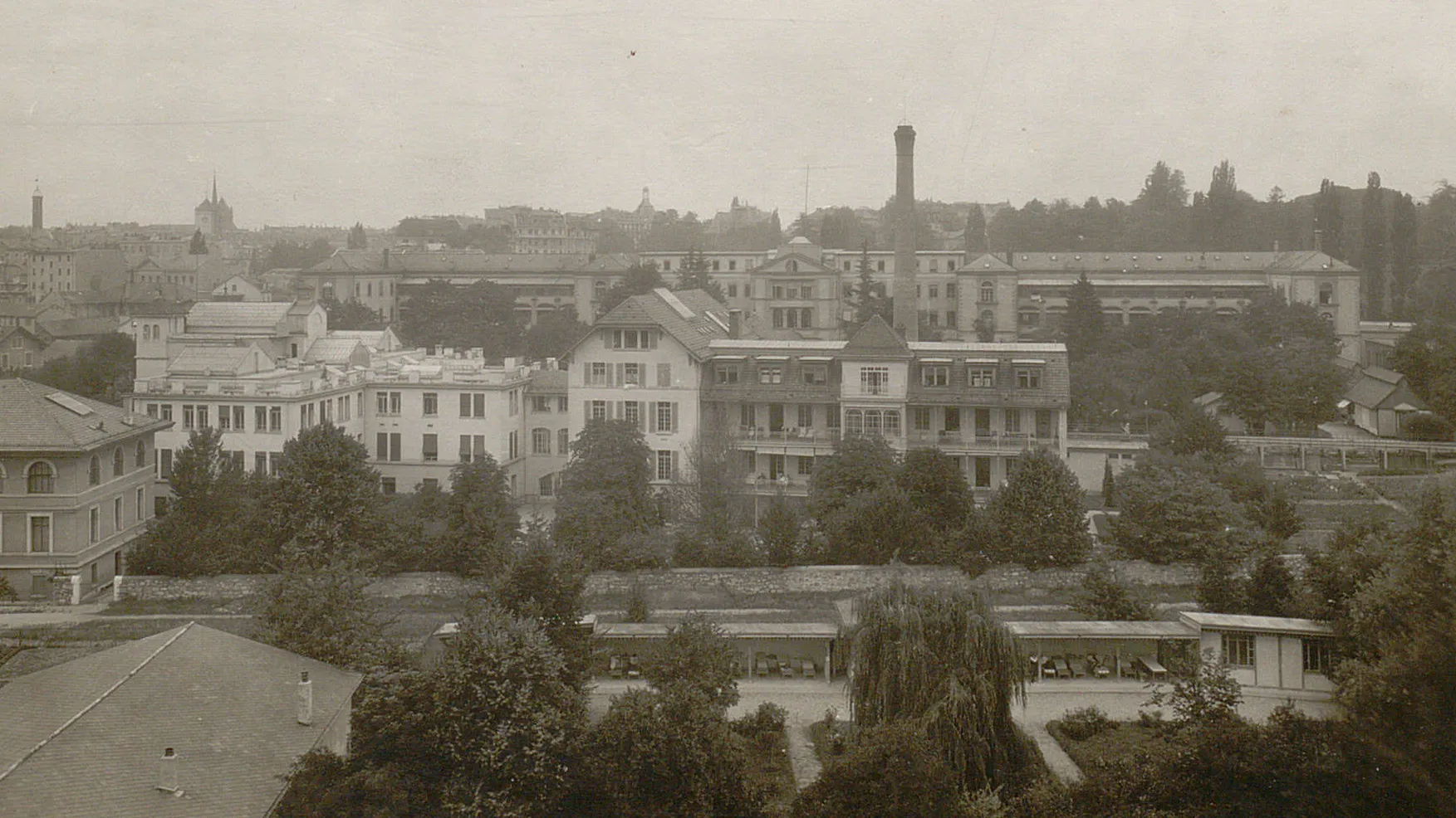 Divers bâtiments, au premier plan une construction basse à toit plat, ouverte sur les côtés, avec des chaises-longues.