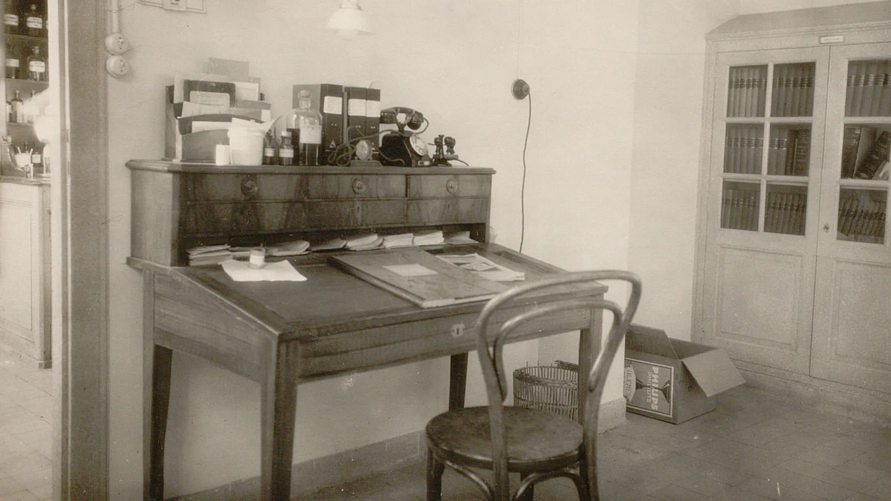 Bureau avec plan de travail incliné, des documents, des tampons, un téléphone. Une chaise.