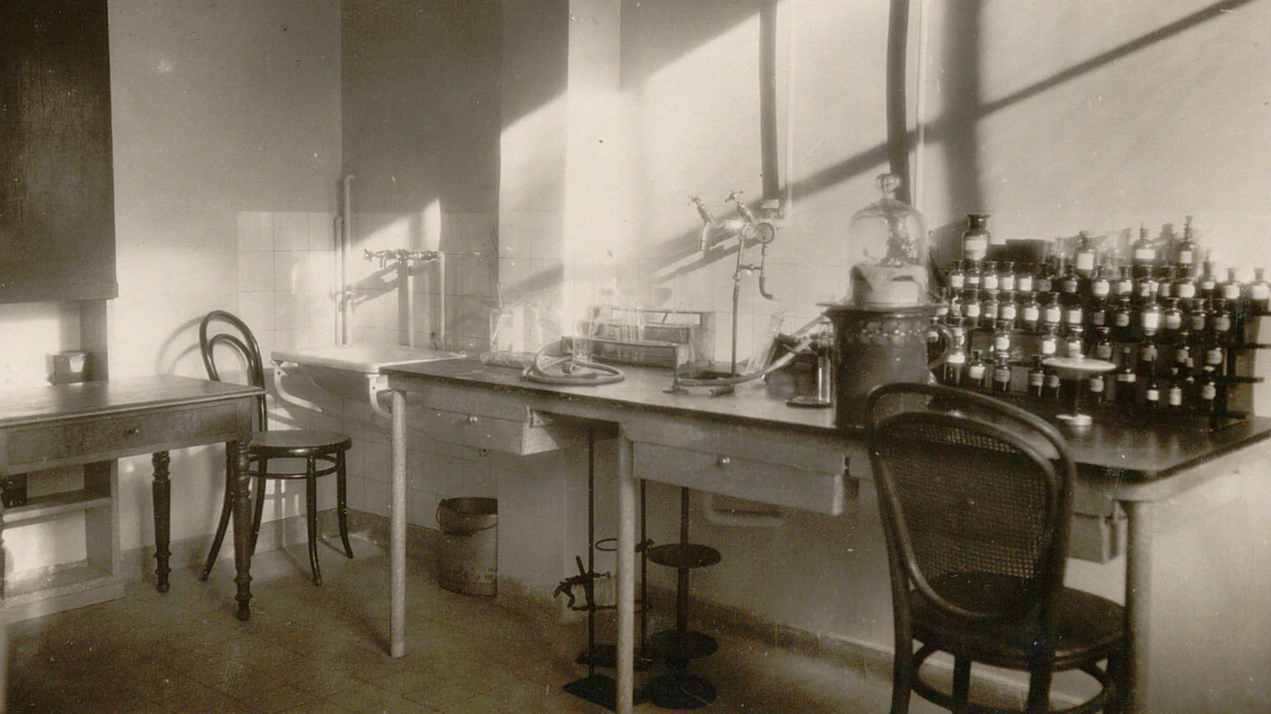 Table de travail avec nombreux flacons, un support à éprouvettes, divers tuyaux et robinets.