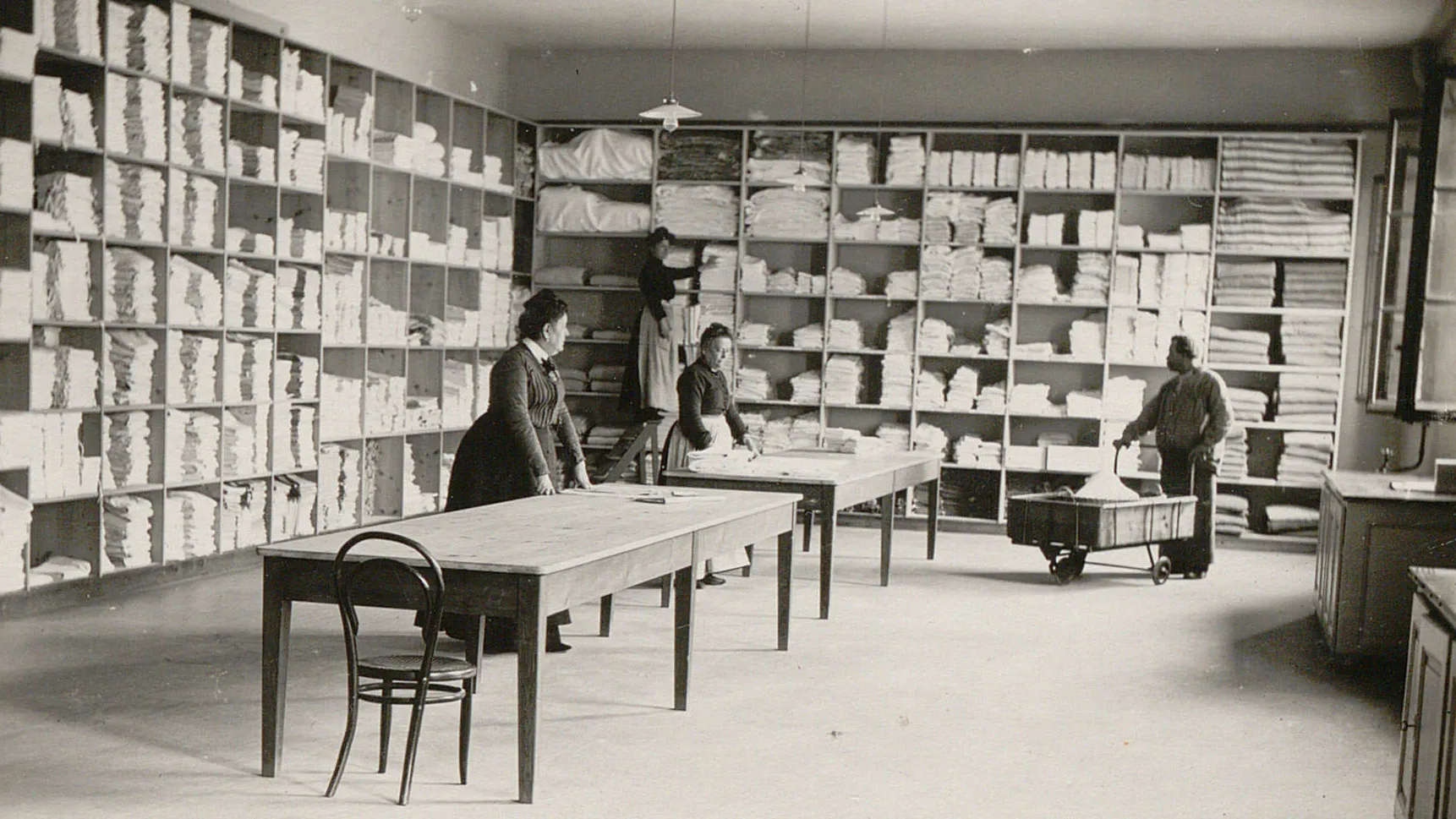 Trois femmes et un homme travaillent pour ranger le linge propre dans des étagères remplies de tas de linge.