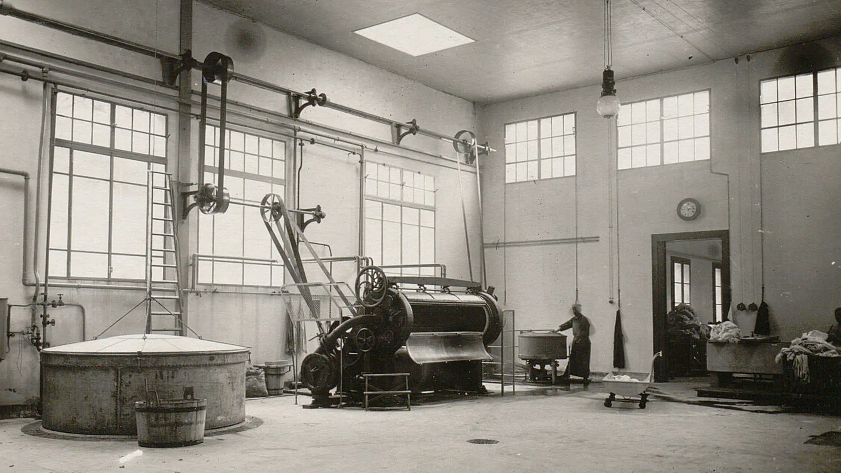 Une énorme machine à laver, ouverte, et plusieurs cuves, des chariots remplis de linge sale.