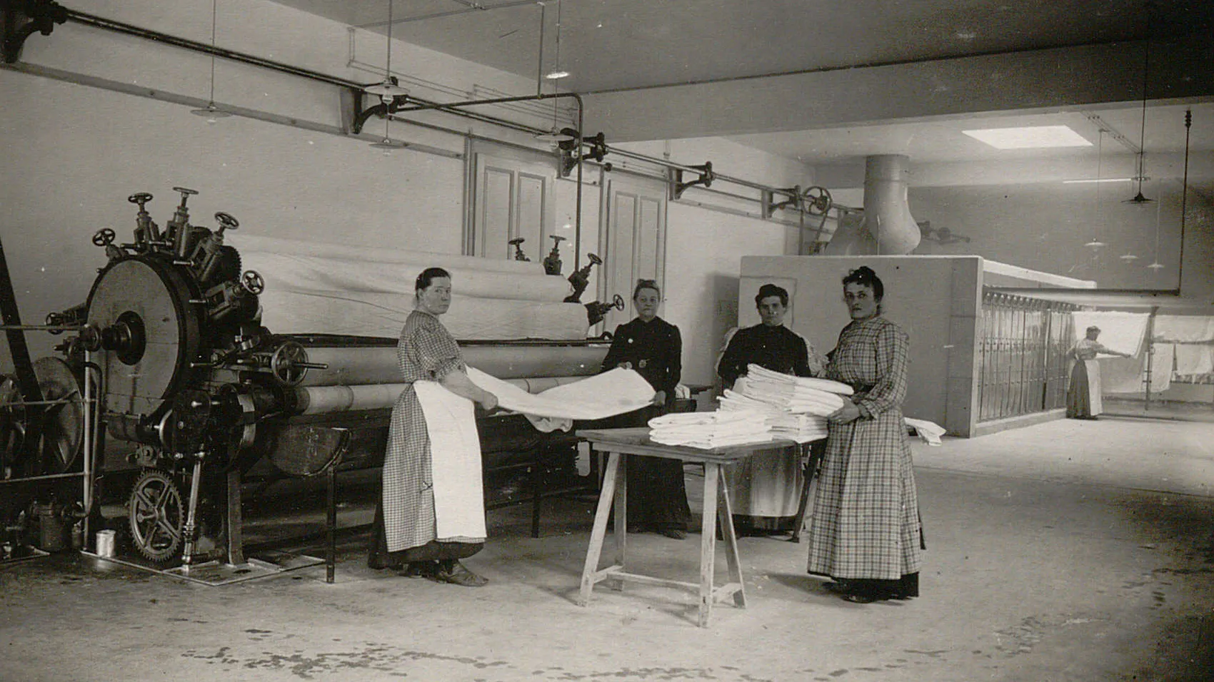 Quatre femmes plient du linge qui sort d'une grande calandre.