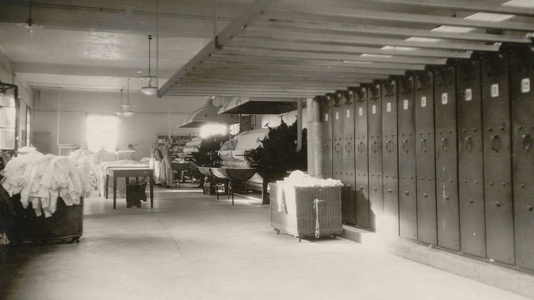 Une grande armoire sèche-linge, plusieurs charriots de linge, au fond deux calandres.