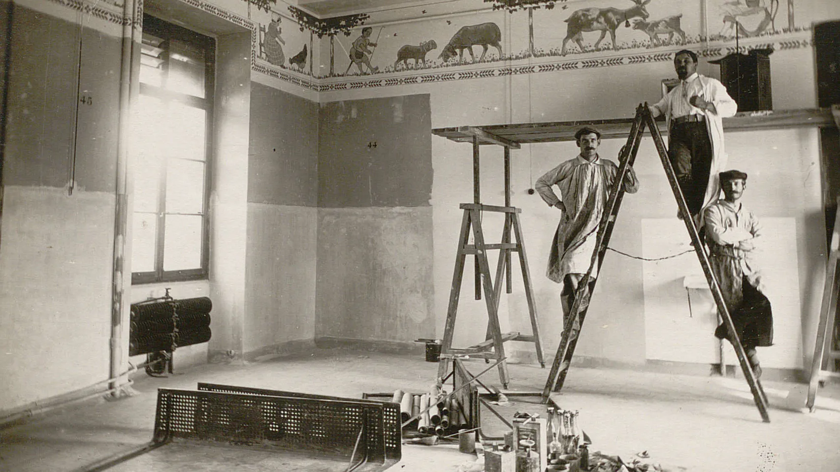Trois hommes (peintres) sur une échelle, en haut des murs il y a une fresque avec des animaux de la ferme.