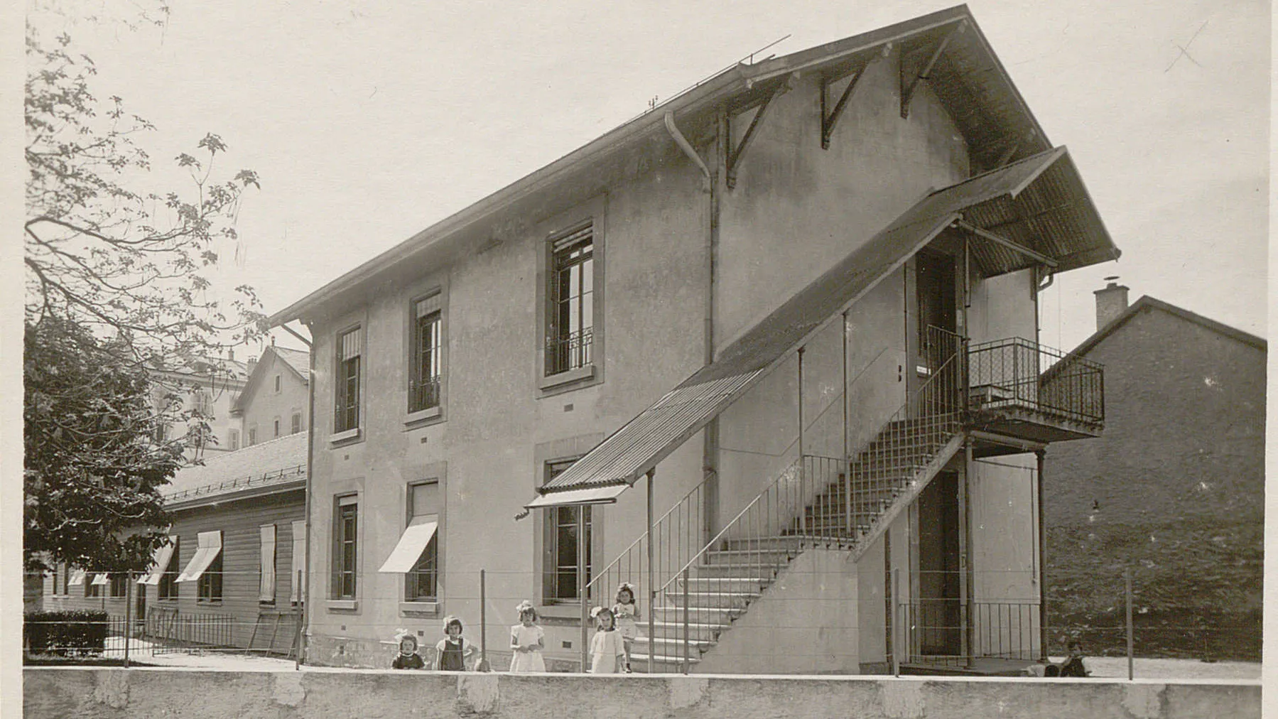 Bâtiment avec un escalier extérieur, cinq filles posent en bas derrière un muret.