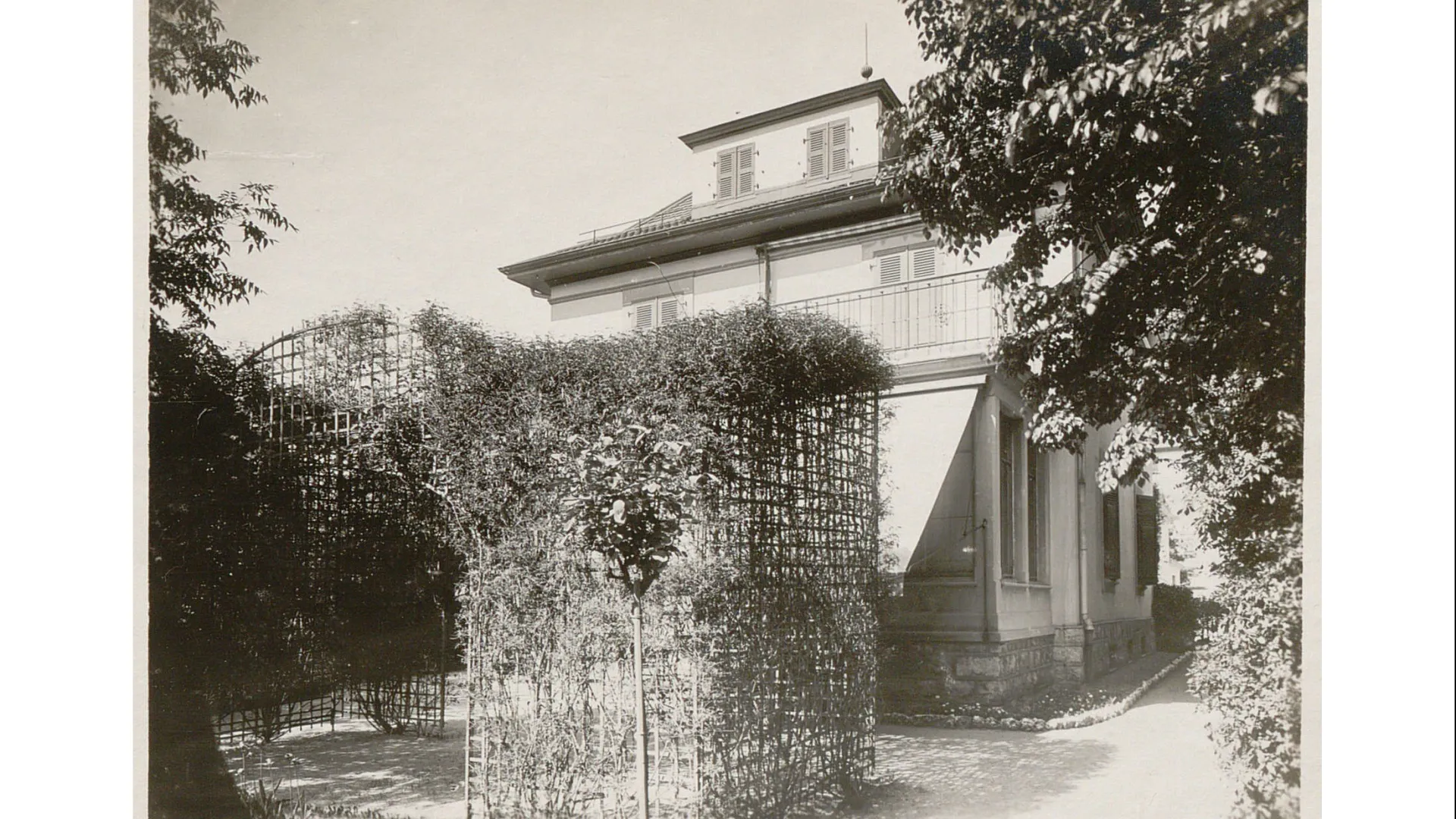 Petite maison, store sur la veranda baissé, treillage entourant la terrasse.