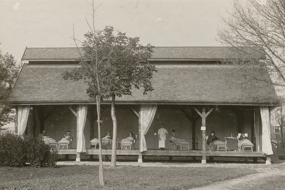 Pavillon sans murs, rideaux ouverts, un infirmier et plusieurs malades dans des chaises-longues.