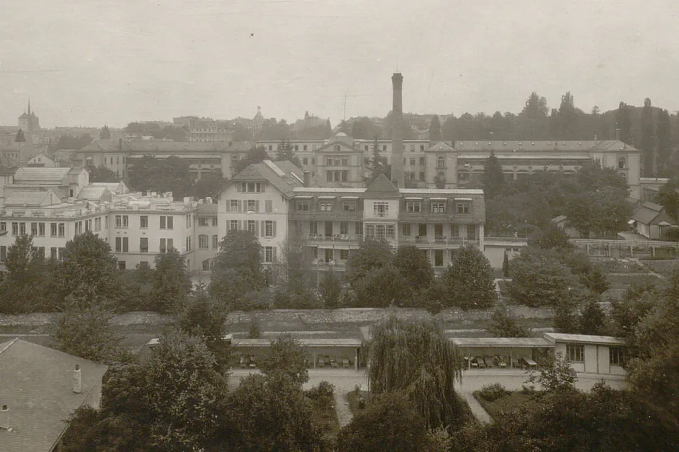 Divers bâtiments, au premier plan une construction basse à toit plat, ouverte sur les côtés, avec des chaises-longues.
