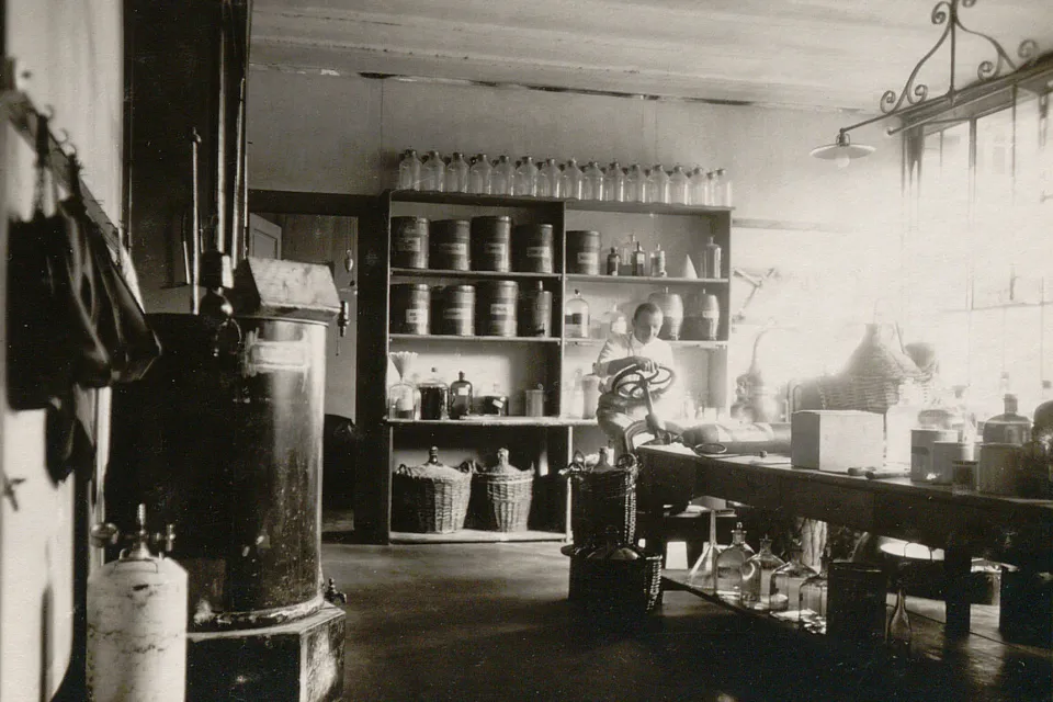 Salle équipée d'étagères remplies de bouteilles et contenants, d'une table de travail, d'un pressoir..