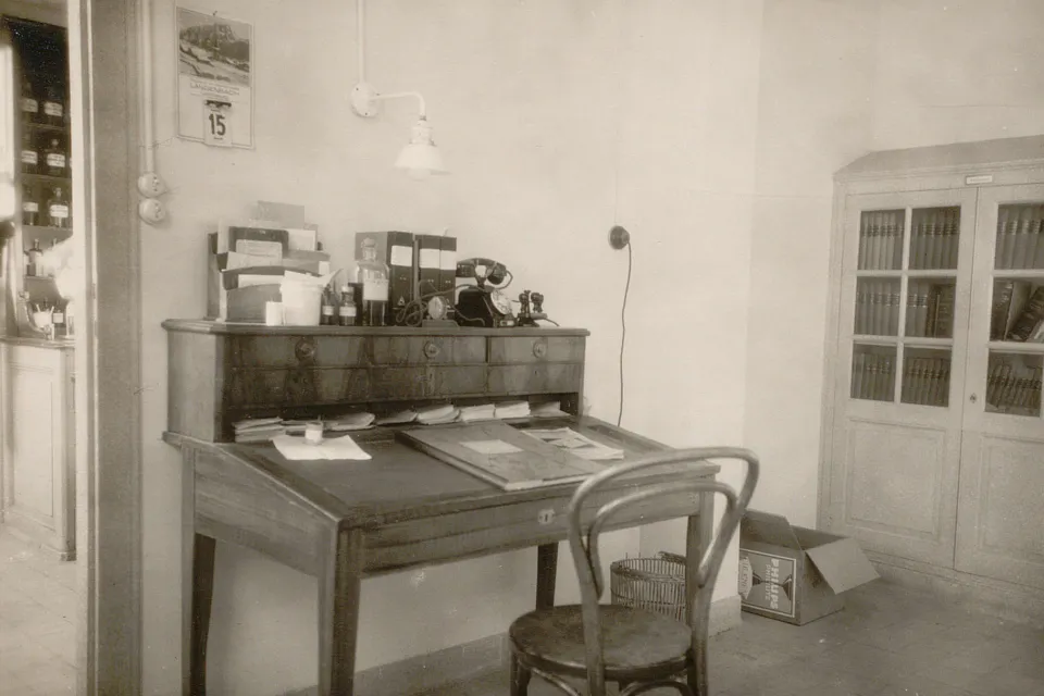 Bureau avec plan de travail incliné, des documents, des tampons, un téléphone. Une chaise.