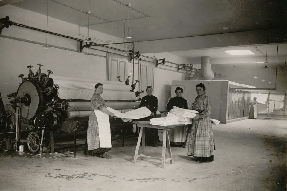 Quatre femmes plient du linge qui sort d'une grande calandre.